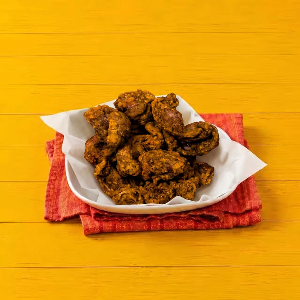 A white bowl filled with crispy, golden-brown fried chicken sits on a red napkin against a yellow wooden background.