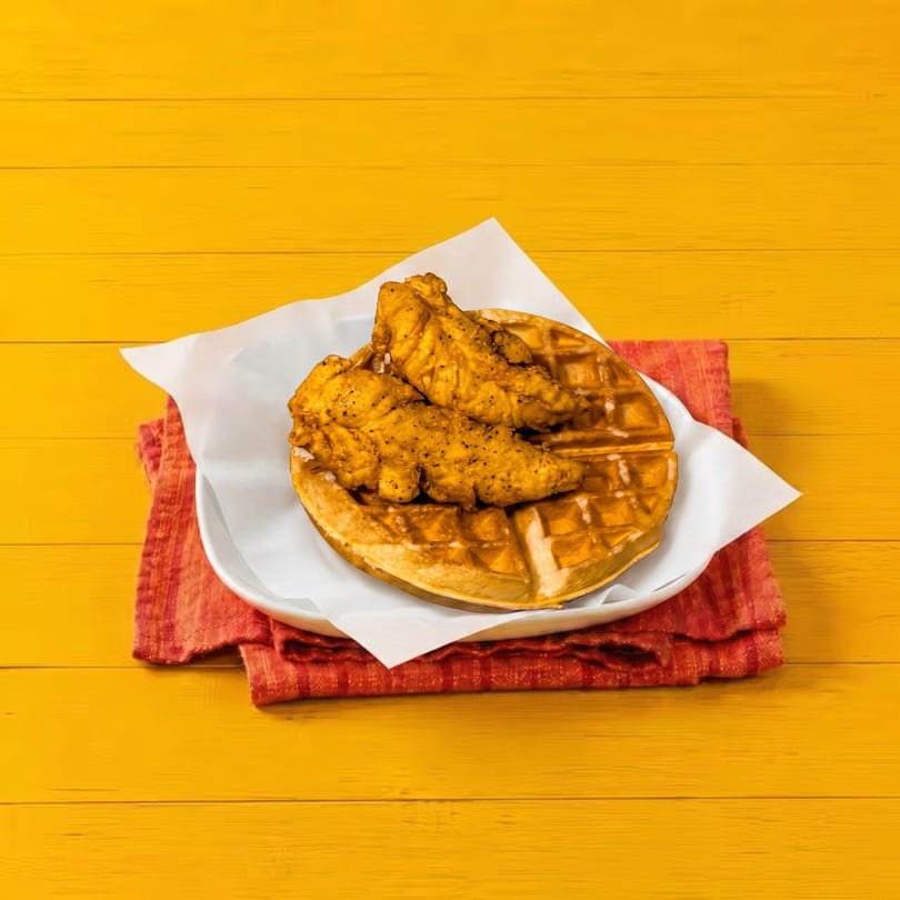 Golden fried chicken tenders on a waffle, served on a white plate with a red napkin.