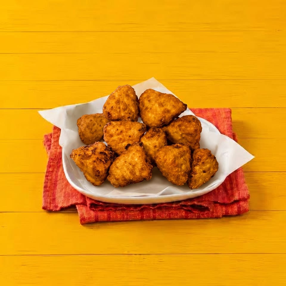 A white plate of golden-brown fried chicken nuggets on a red napkin, against a yellow wooden background.